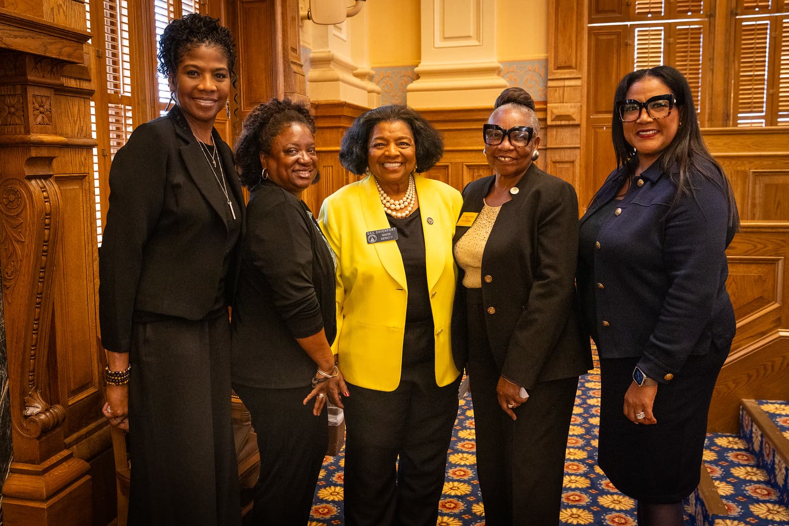 Senator Gail Davenport in a yellow blazer poses with four women in an ornate room.