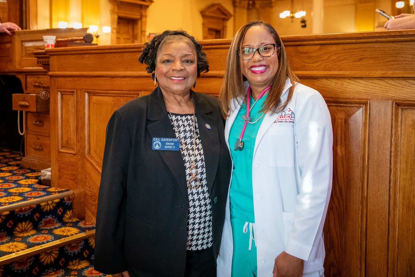 Senator Gail Davenport and a medical professional in a white lab coat smile together.