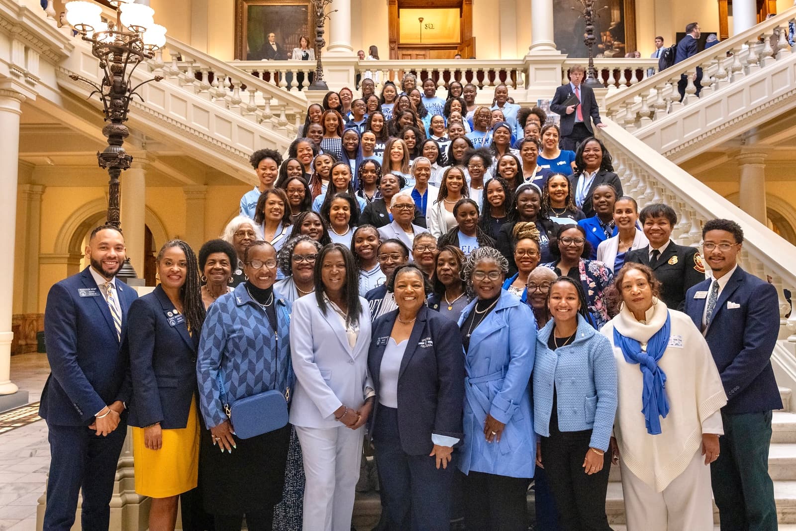 Large group of Black women in blue and white attire posing on grand marble stairs.