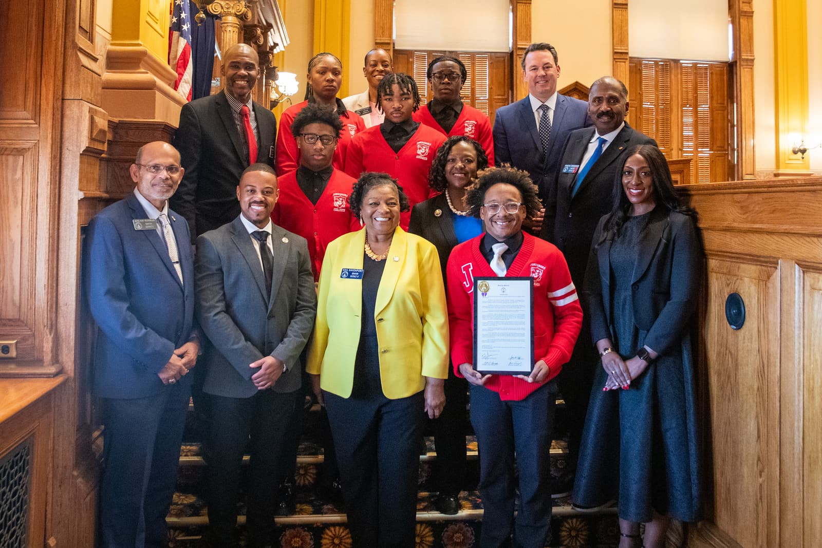 Diverse group of professionals and students in red sweaters pose with a framed award certificate.