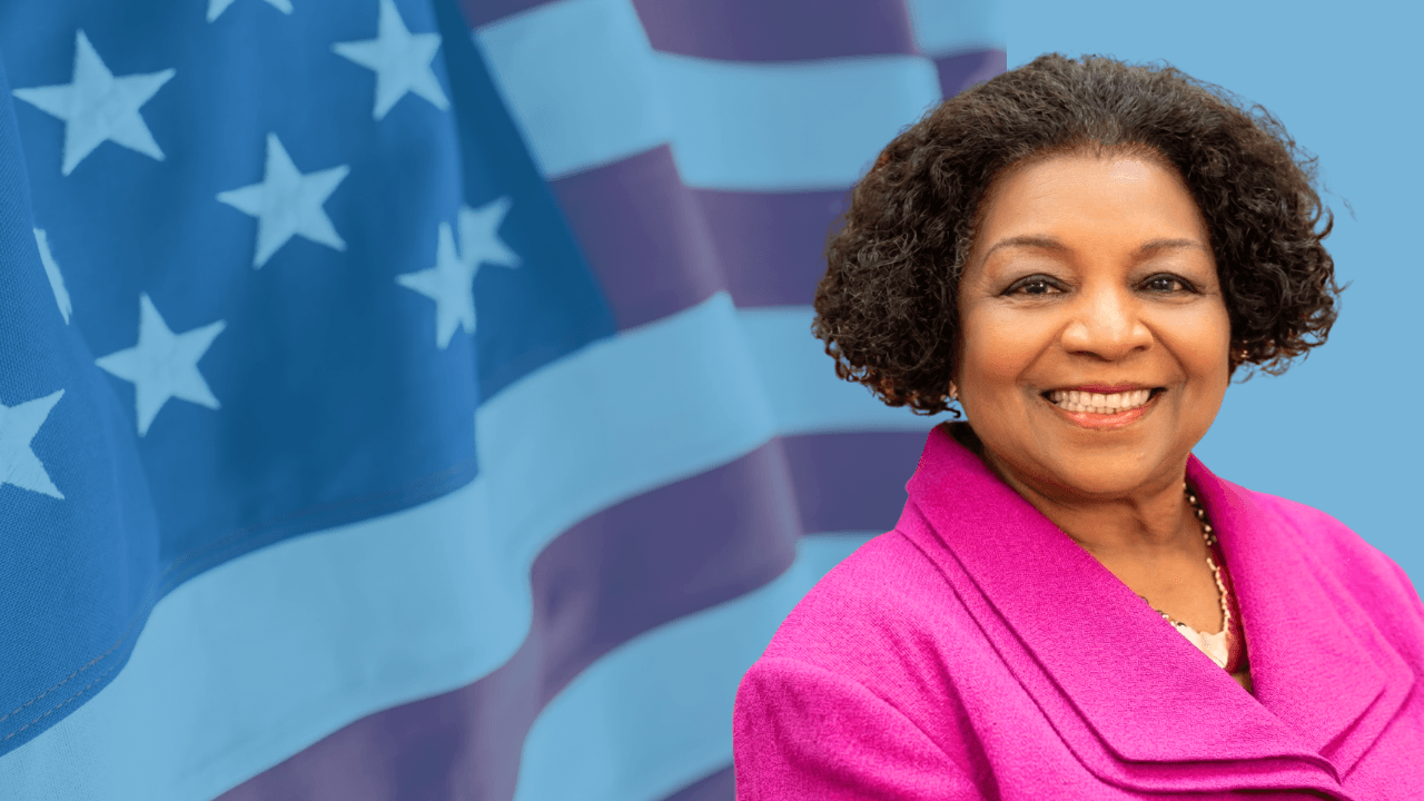 Smiling Black woman in a pink blazer against a stylized blue American flag background.